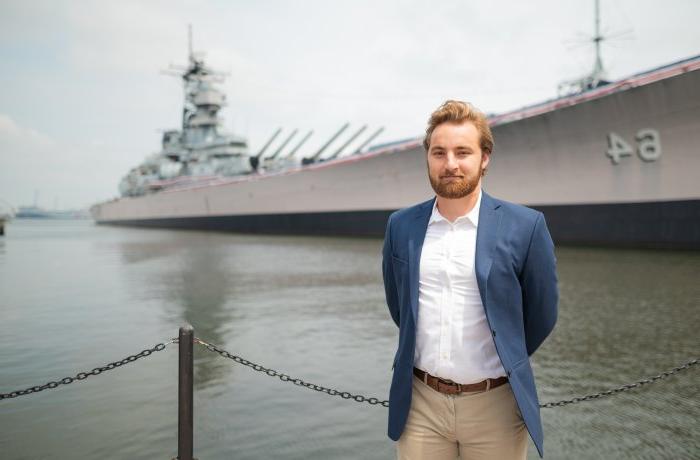 A young man stands on a pier by the Battleship Wisconsin in Nofolk.